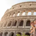 Una pareja conformada por un hombre y mujer abrazados al frente del Coliseo de Roma