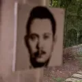 La fotografía de Tomás Nativí, esposo desaparecido de Berta Oliva, enmarca a su fundadora mientras camina hacia él por los jardines del Hogar contra el Olvido, en Santa Ana, Honduras. Nativí fue detenido arbitrariamente y desaparecido el 11 de junio de 1981.