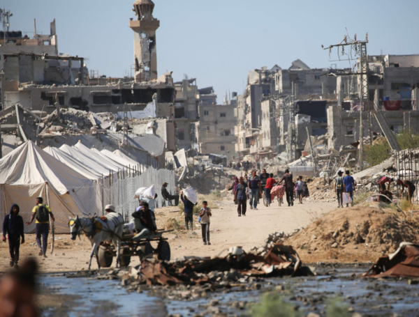 Displaced Palestinians walk past tents and destroyed buildings as they return to their homes in the in al-Zahra area, north of the Nuseirat refugee camp in the central Gaza Strip, on October 14, 2025, a day after a ceasefire came into effect. The US president hailed a "tremendous day for the Middle East" as he and regional leaders signed a declaration on October 13, 2025 meant to cement a ceasefire in Gaza, hours after Israel and Hamas exchanged hostages and prisoners. (Photo by Eyad BABA / AFP)