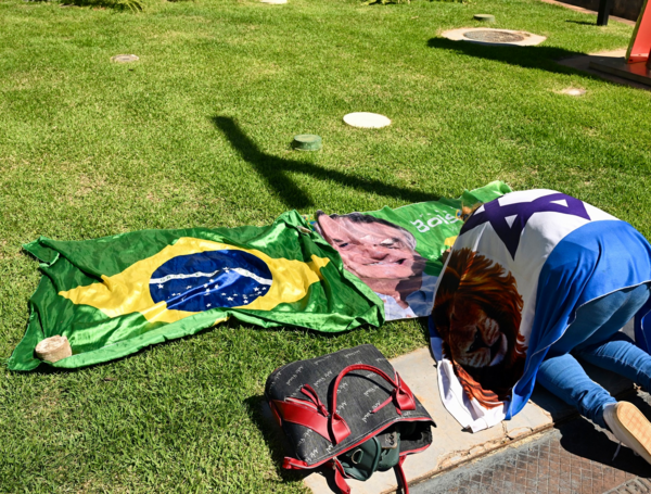 Un simpatizante del expresidente brasileño (2029-2023) Jair Bolsonaro, envuelto en una bandera israelí, reza junto a una bandera brasileña frente al Hospital DF Star