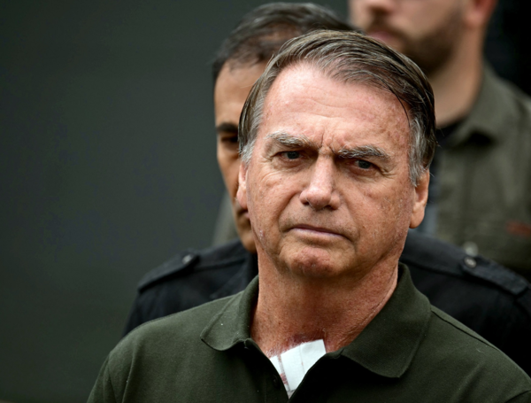 Un simpatizante del expresidente brasileño (2029-2023) Jair Bolsonaro, envuelto en una bandera israelí, reza junto a una bandera brasileña frente al Hospital DF Star