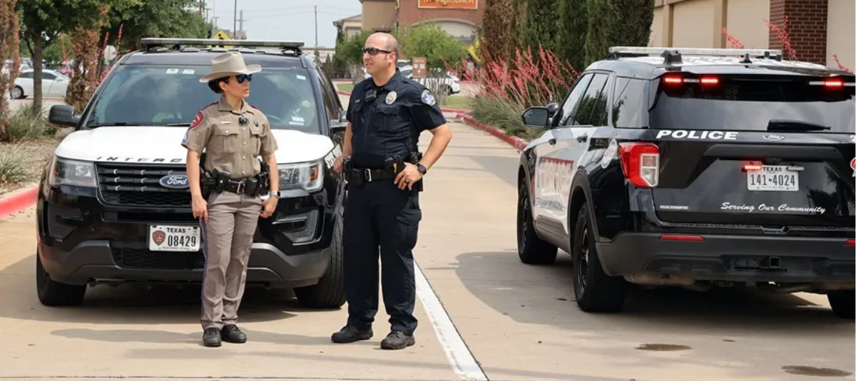 Un policía estatal (i) y un policía de la ciudad de Allen (d) conversan mientras bloquean la entrada al Allen Premium Outlet Mall.