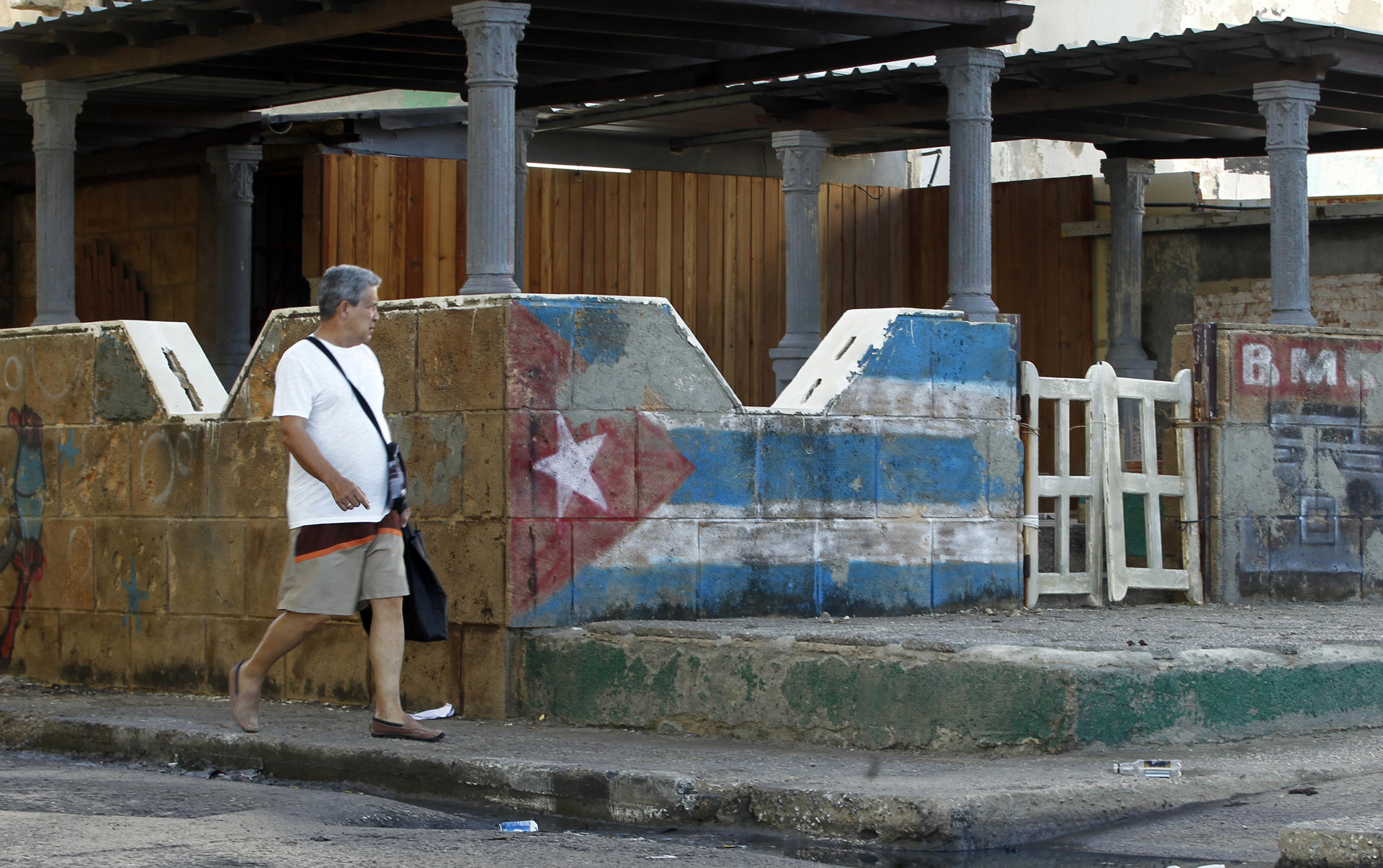 Un hombre camina en La Habana junto a una pintura de la bandera de Cuba