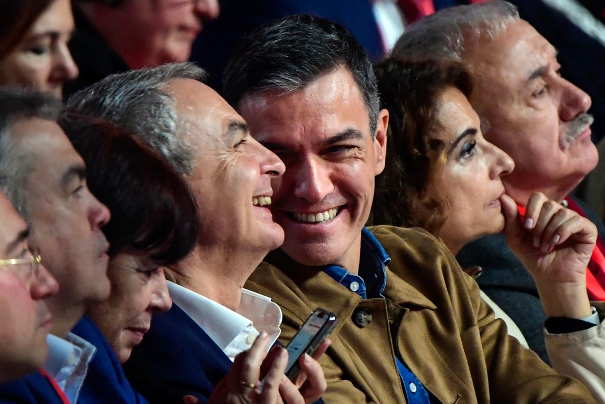 El presidente del Gobierno español, Pedro Sánchez, sonríe junto al expresidente del Gobierno José Luis Rodríguez Zapatero.