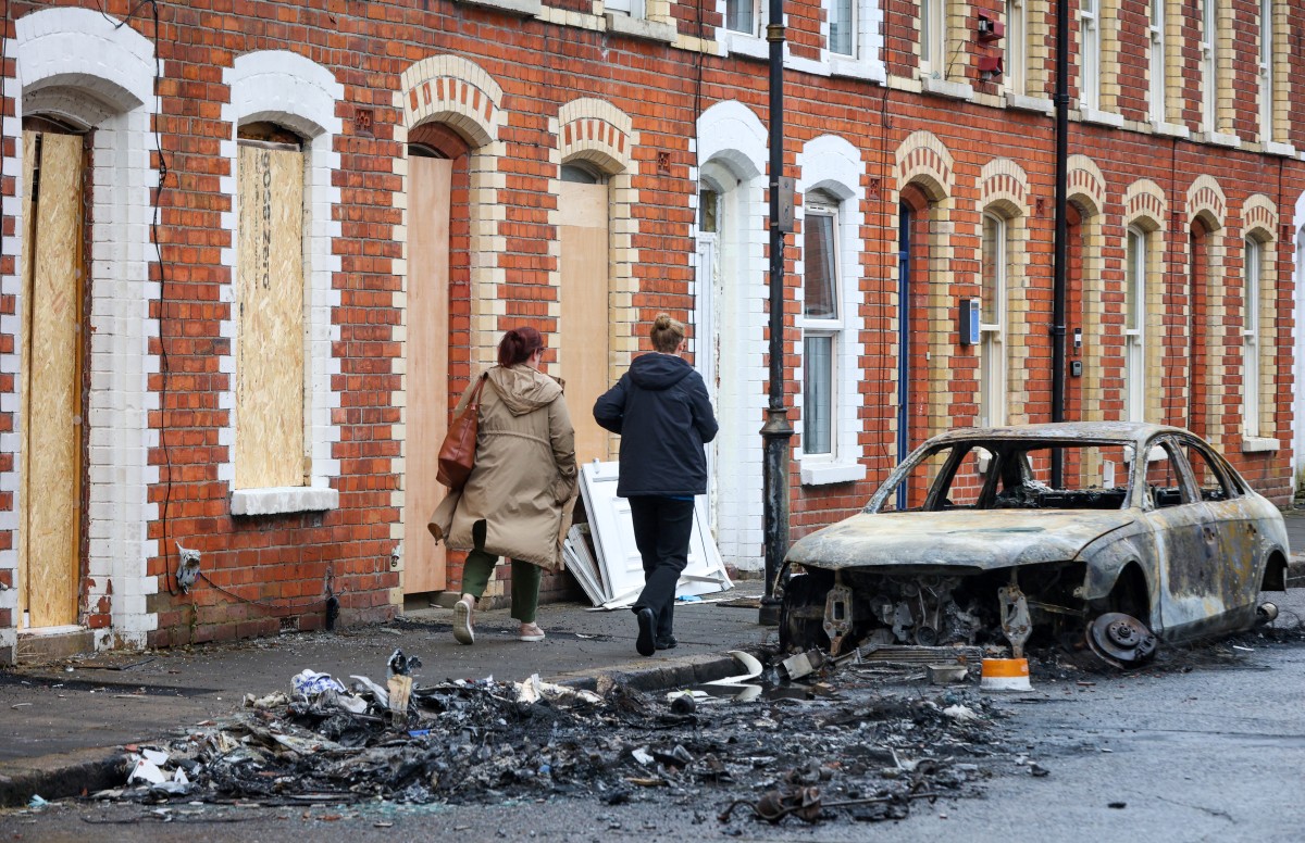Personas caminan junto a un coche calcinado en Newtownards Road, Belfast, Irlanda del Norte, el 11 de junio de 2026