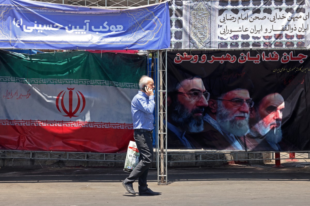 Un hombre pasa junto a la bandera nacional de Irán y una pancarta con las imágenes del difunto fundador de la Revolución Islámica, Ruhollah Jomeini (derecha).