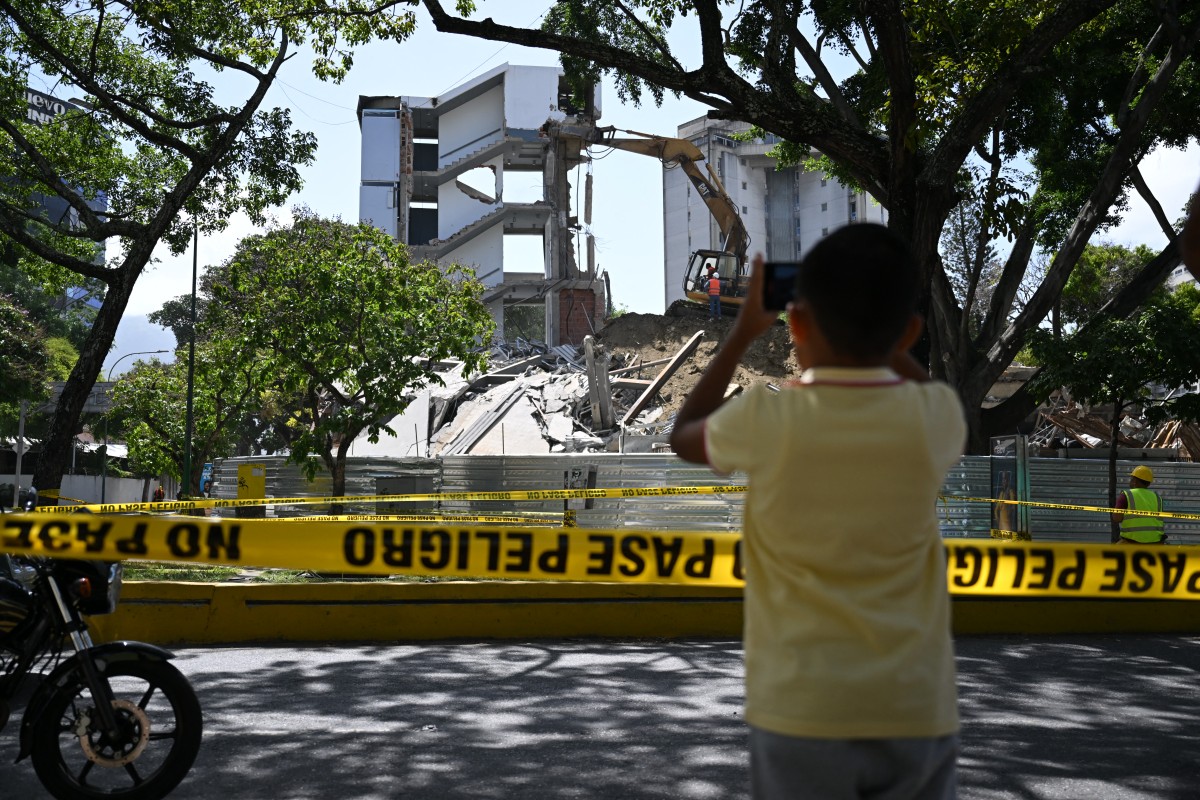 Persona toma una fotografía de un edificio mientras es demolido en Caracas, Venezuela, tras los terremotos del 24 de junio