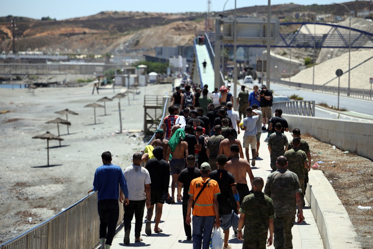 Un grupo de migrantes se acerca al puesto fronterizo para regresar a Marruecos, escoltados por soldados de infantería españoles, en el enclave español de Ceuta, en el norte de África