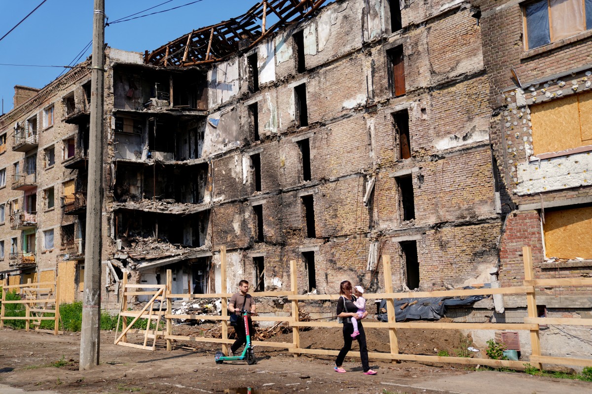 Una pareja y un niño pasan junto a un edificio de apartamentos gravemente dañado tras los ataques rusos en el distrito de Lukianivska de Kiev